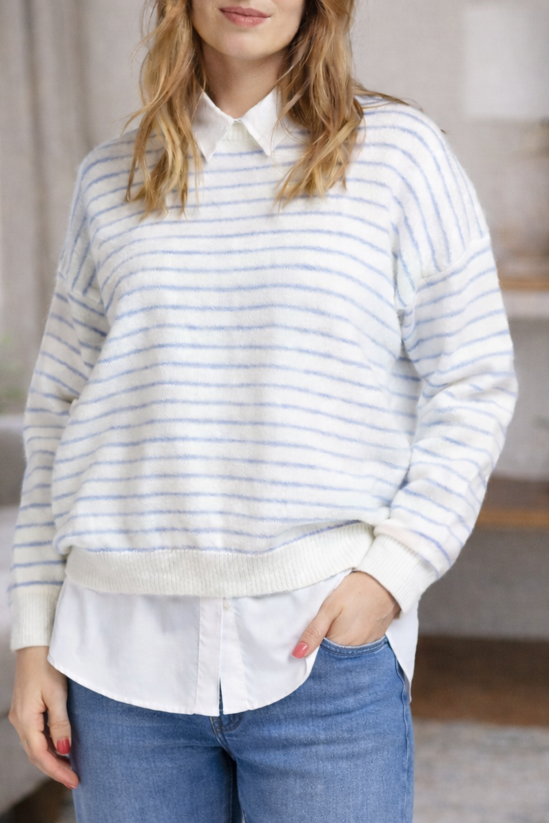 Pull crème à fines rayures ciel porté en superposition sur une chemise blanche, col et bas visibles pour un style actuel.