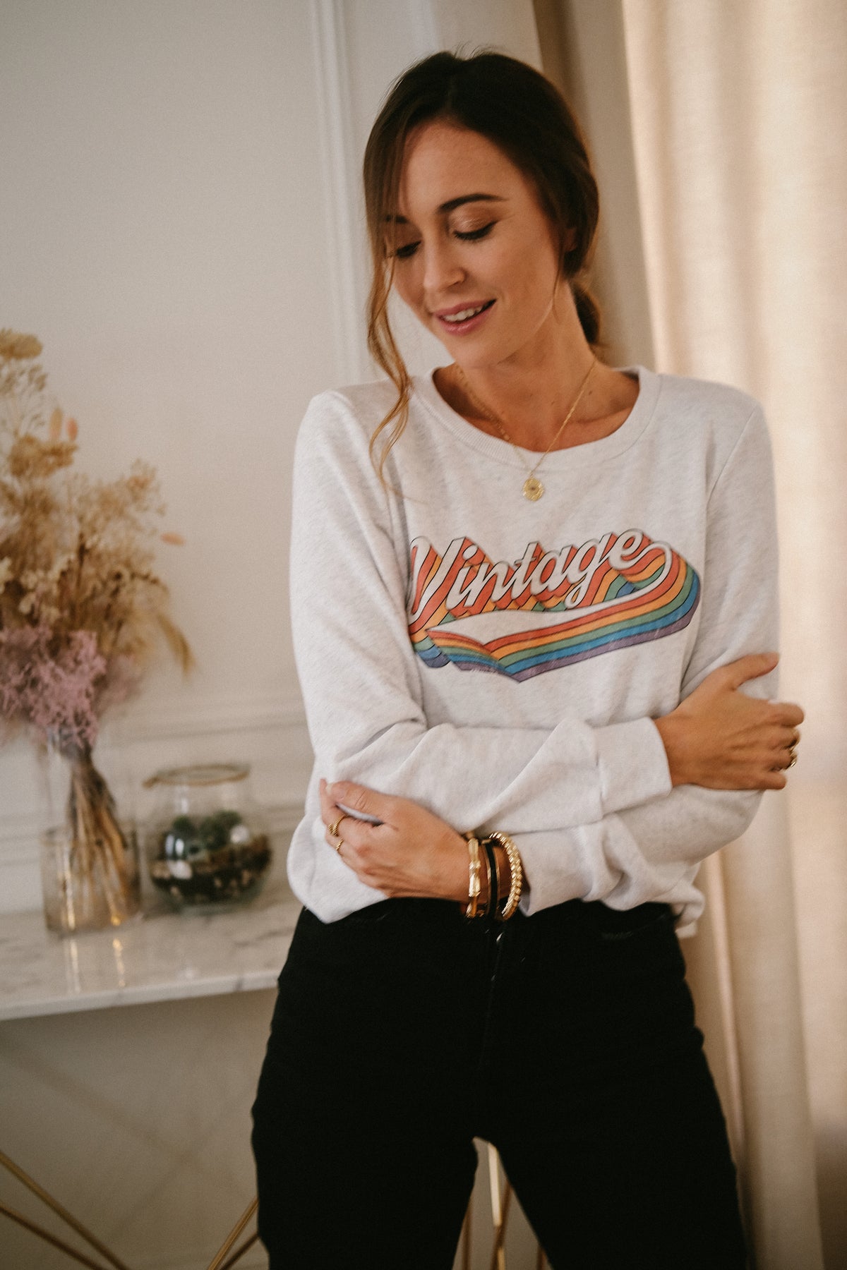 Look femme porté du sweat VINTAGE gris chiné à imprimé coloré, associé à un pantalon noir pour une tenue décontractée mais féminine de Jubylee